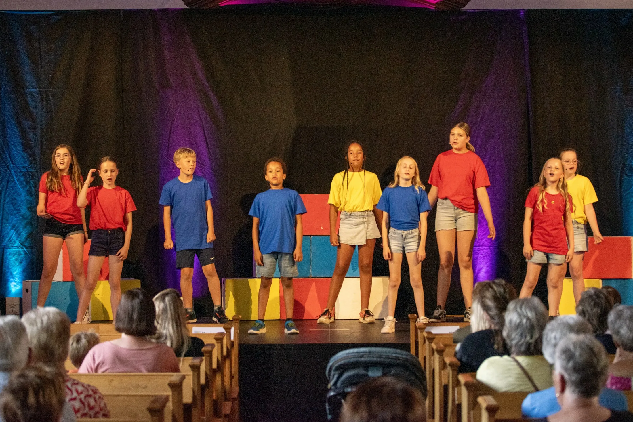 De kids van MusicalKids staan in een rij voor een kerk vol publiek